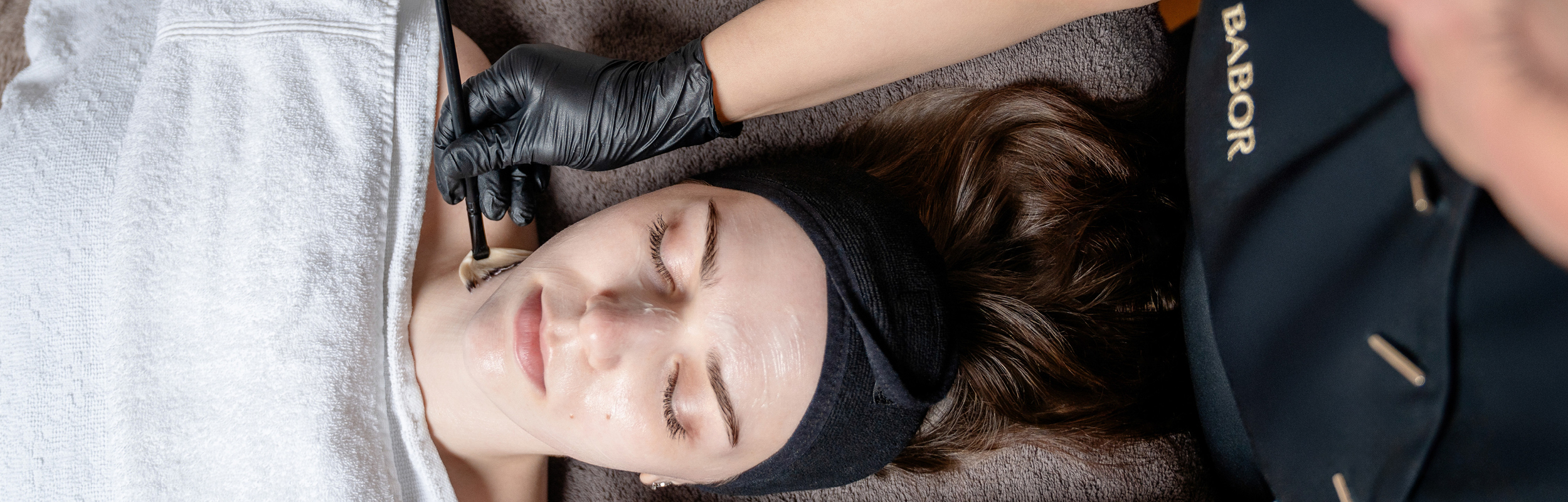 Kosmetikerin behandelt Kundin und trägt Produkt im Gesicht mit einem Pinsel auf.